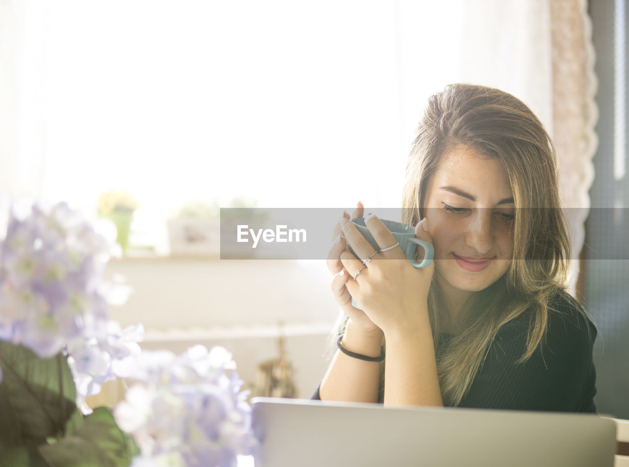 YOUNG WOMAN USING MOBILE PHONE IN LAPTOP