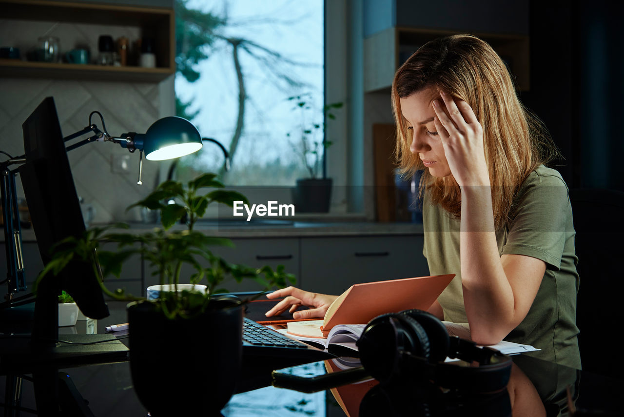 Tired woman works late at home workplace in the night