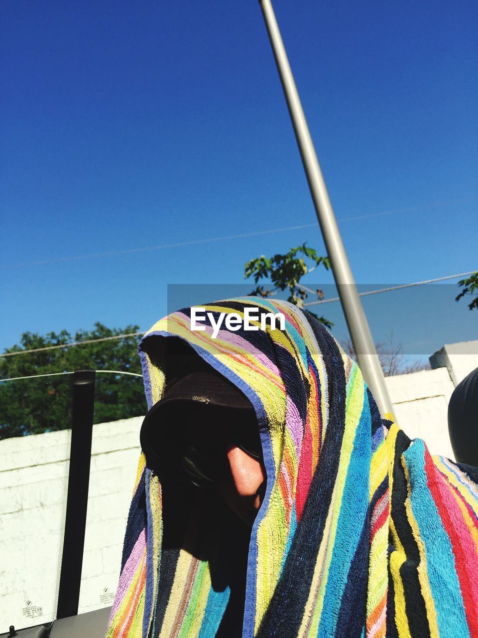 Person covering face with towel against clear blue sky on sunny day