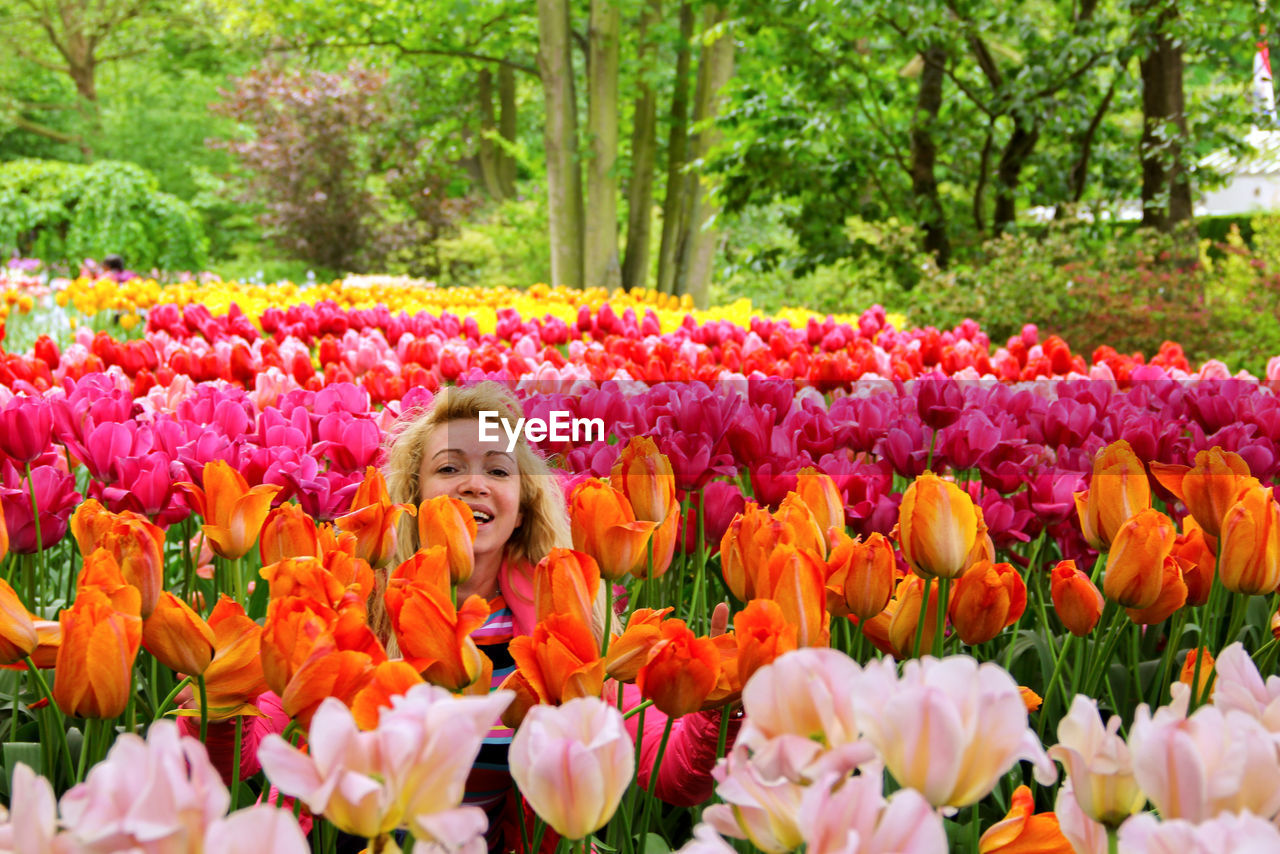 Portrait of happy woman sitting amidst multi colored tulips in garden