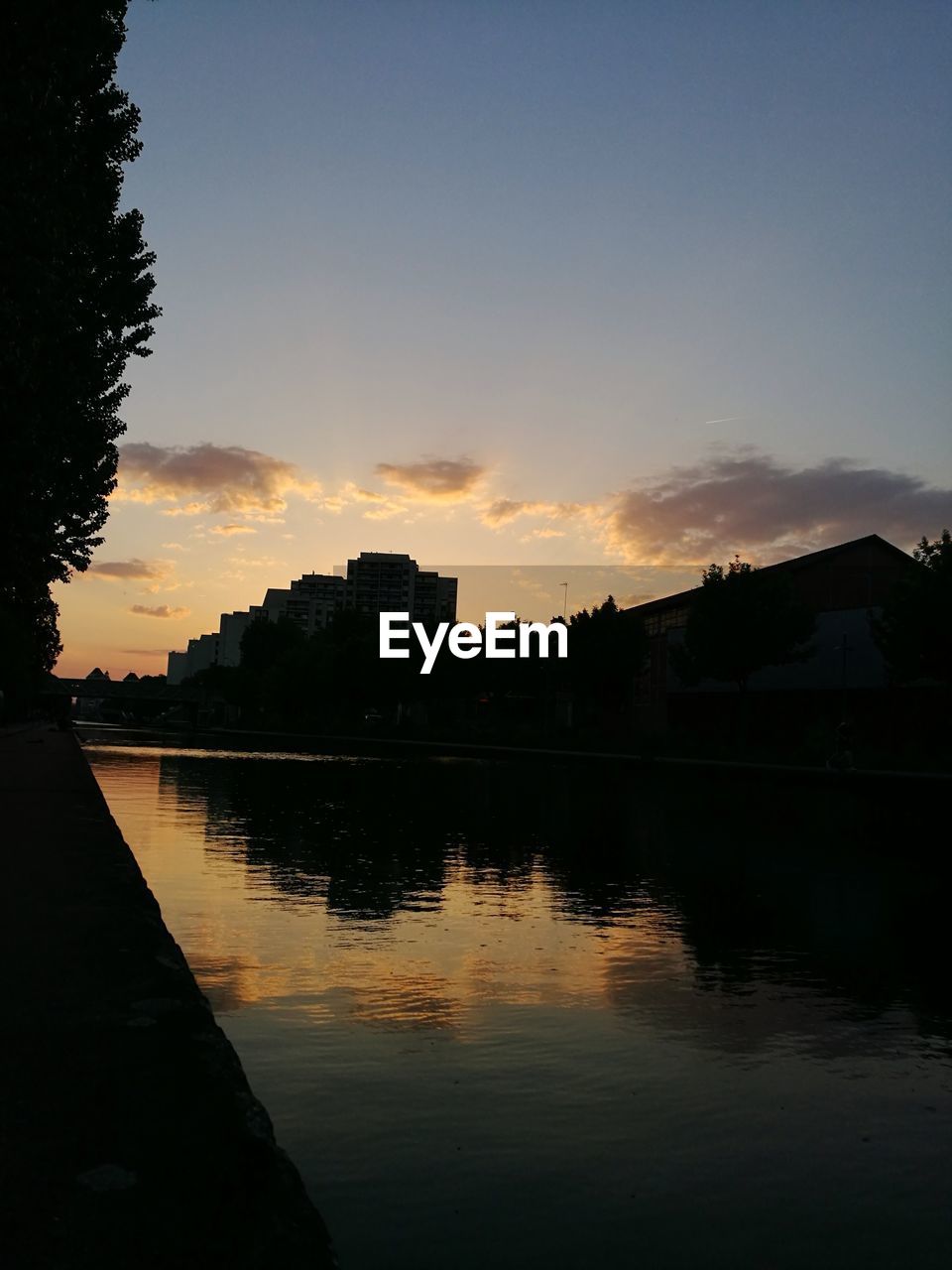 SCENIC VIEW OF LAKE BY BUILDINGS AGAINST SKY DURING SUNSET