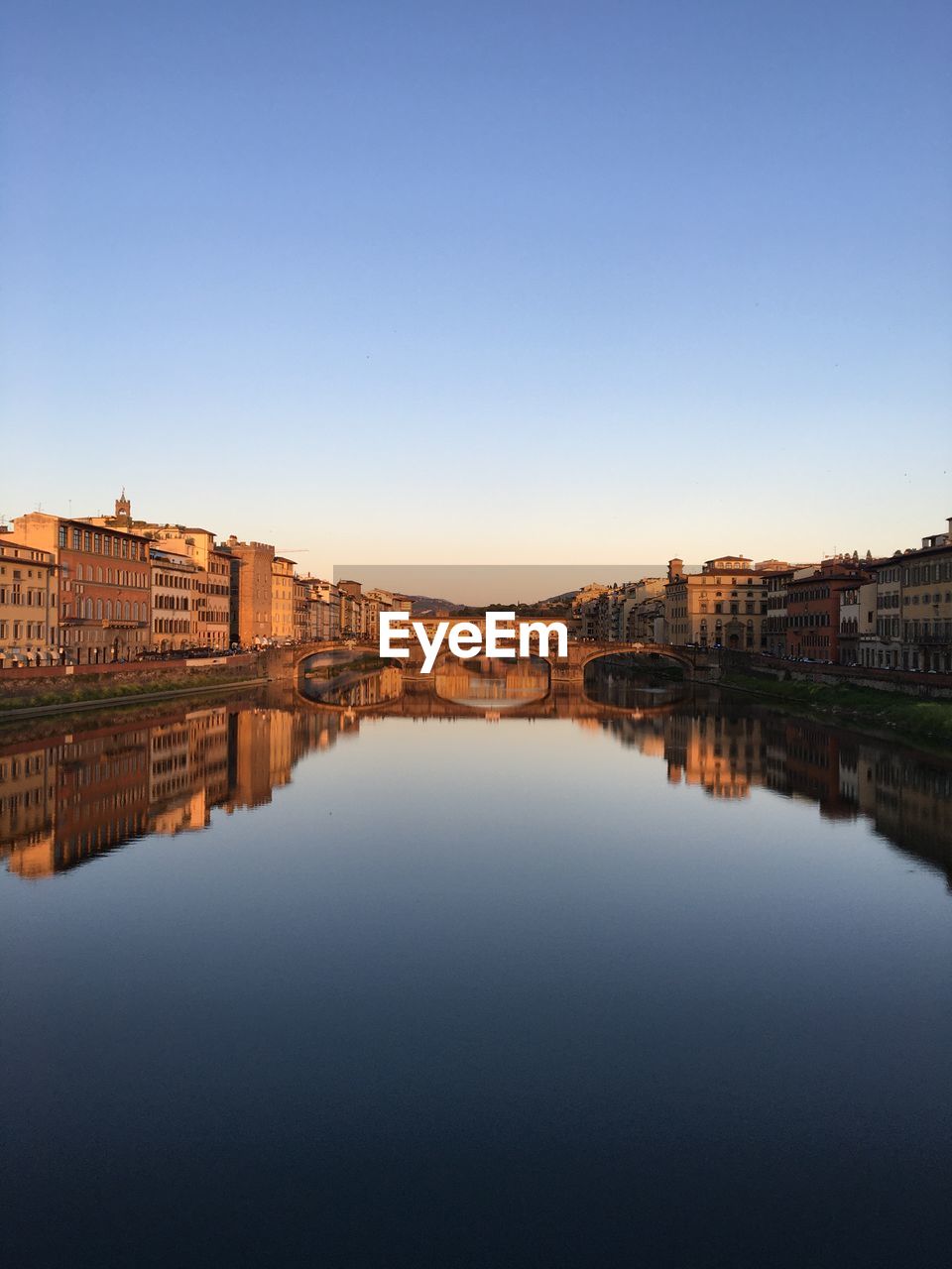 Reflection of buildings in river against clear blue sky