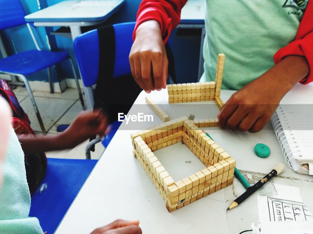 Midsection of people creating art product with toy blocks on table 