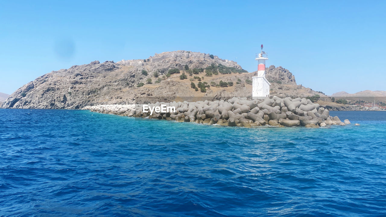 lighthouse, water, sea, sky, blue, tower, nature, ocean, architecture, travel destinations, clear sky, guidance, land, scenics - nature, coast, travel, built structure, no people, islet, day, rock, building exterior, beauty in nature, building, beach, mountain, island, bay, outdoors, sunny, coastline, shore, tourism, environment, flag, cove, tranquil scene, landscape, waterfront, vacation, tranquility