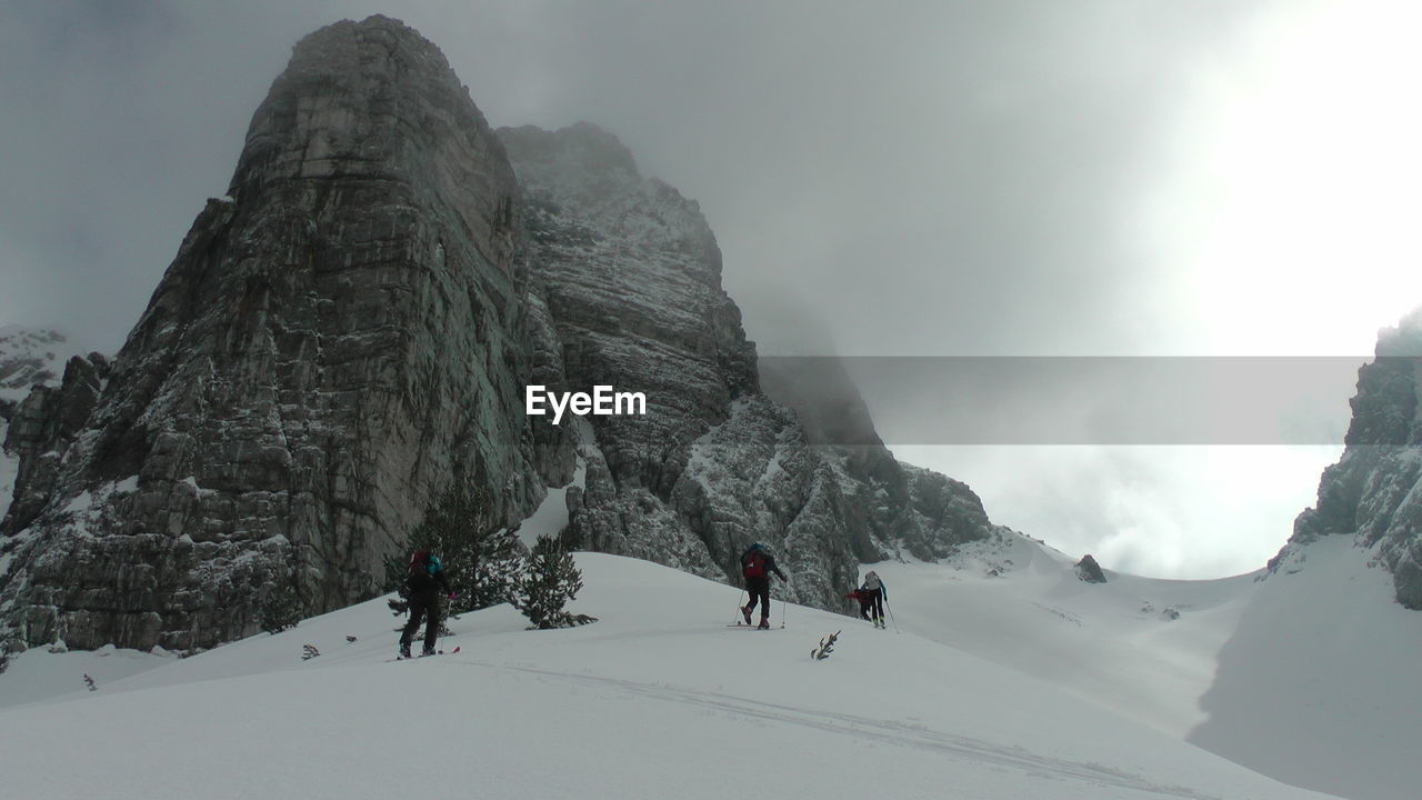 Low angle view of people hiking on snow covered mountain against sky
