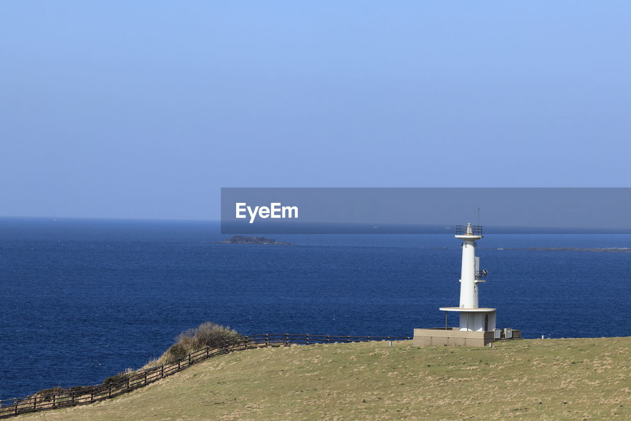 Lighthouse by sea against clear blue sky