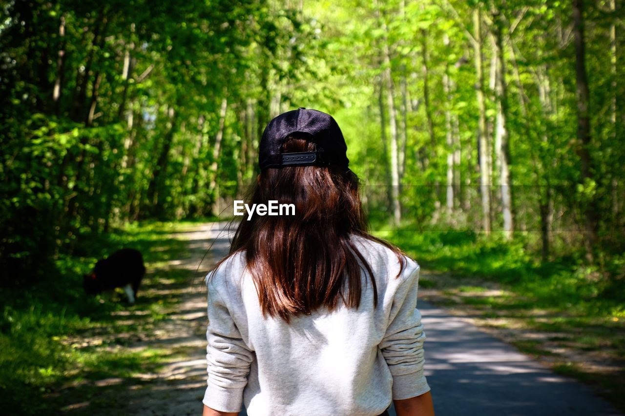 Rear view of young woman wearing cap walking on road in forest