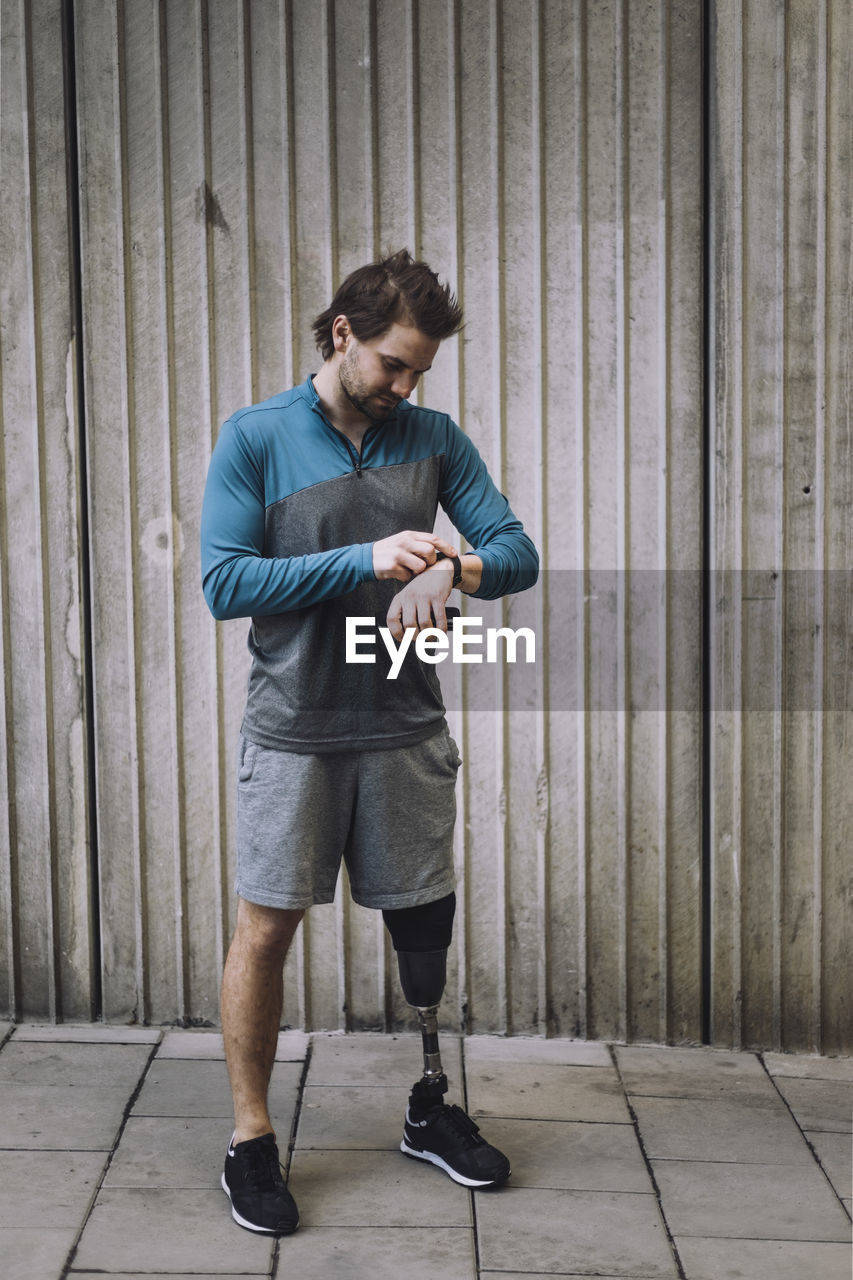 Young man with disability checking time while standing on footpath against wall