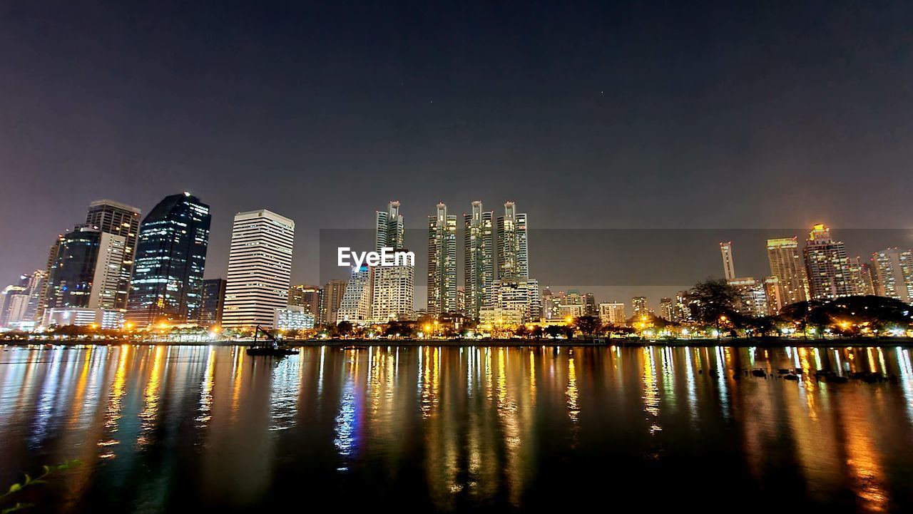 ILLUMINATED MODERN BUILDINGS BY RIVER AGAINST SKY