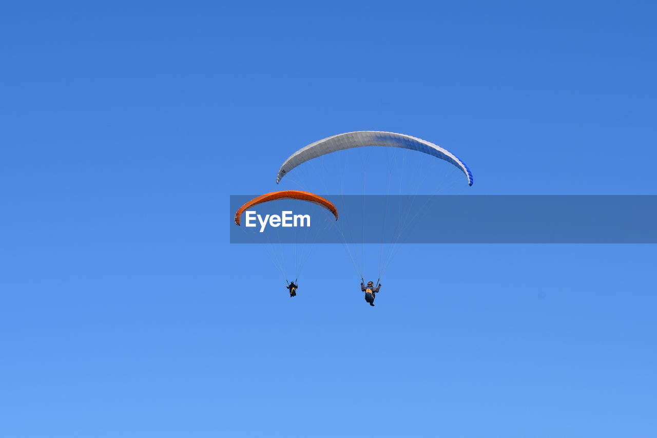 LOW ANGLE VIEW OF PERSON FLYING KITE AGAINST BLUE SKY