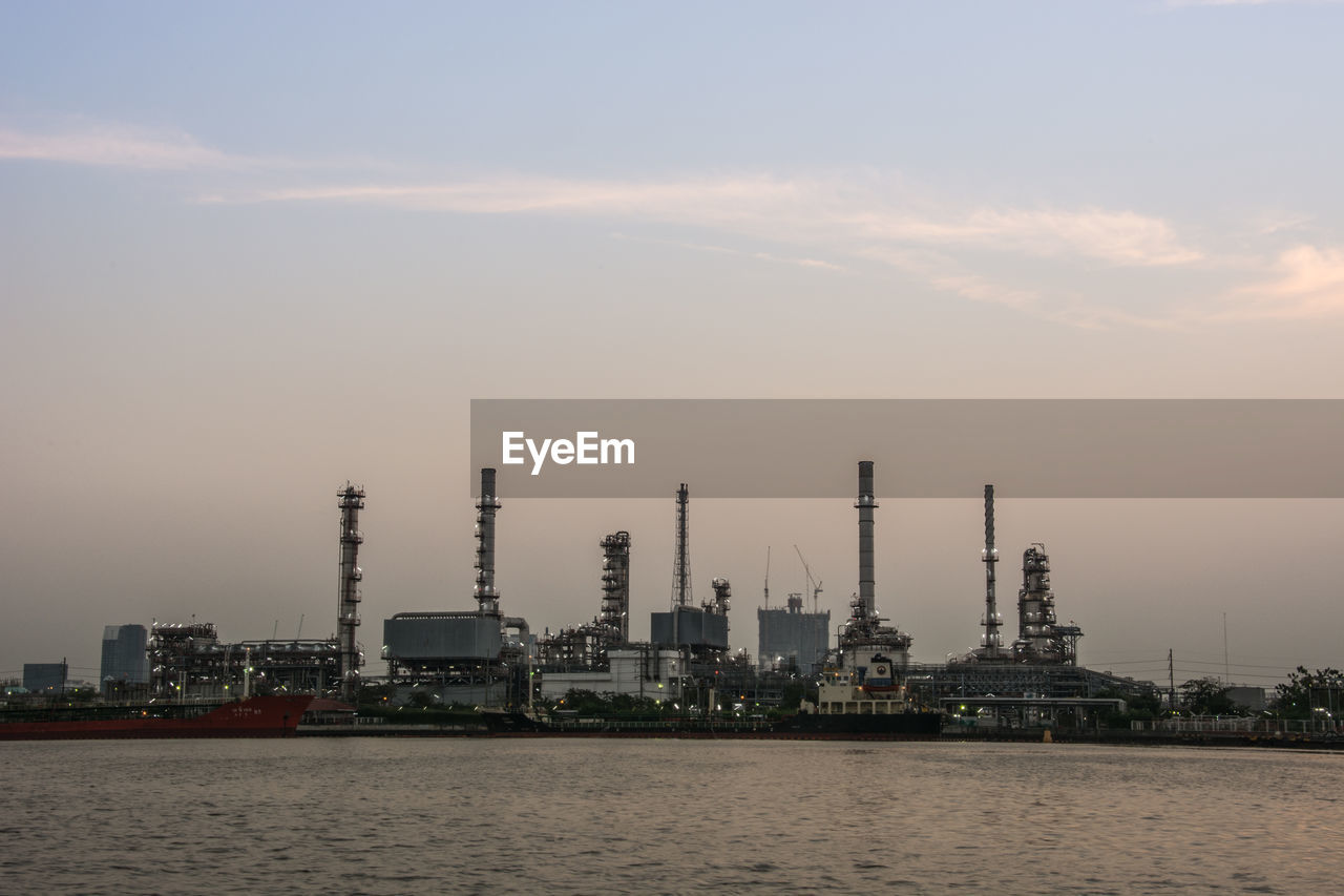 View of oil refinery by sea during sunset against sky
