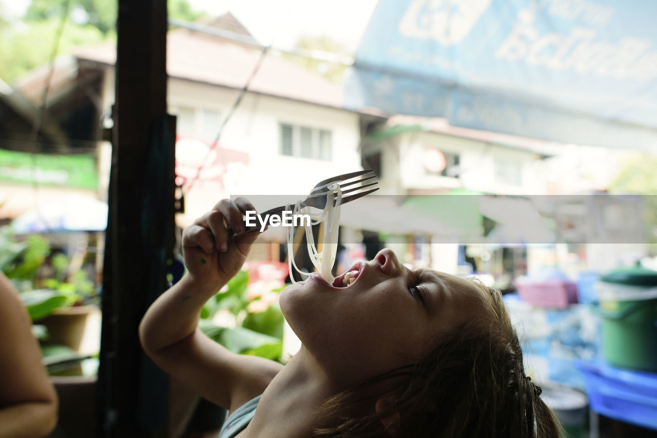 Side view of girl eating noodles in restaurant