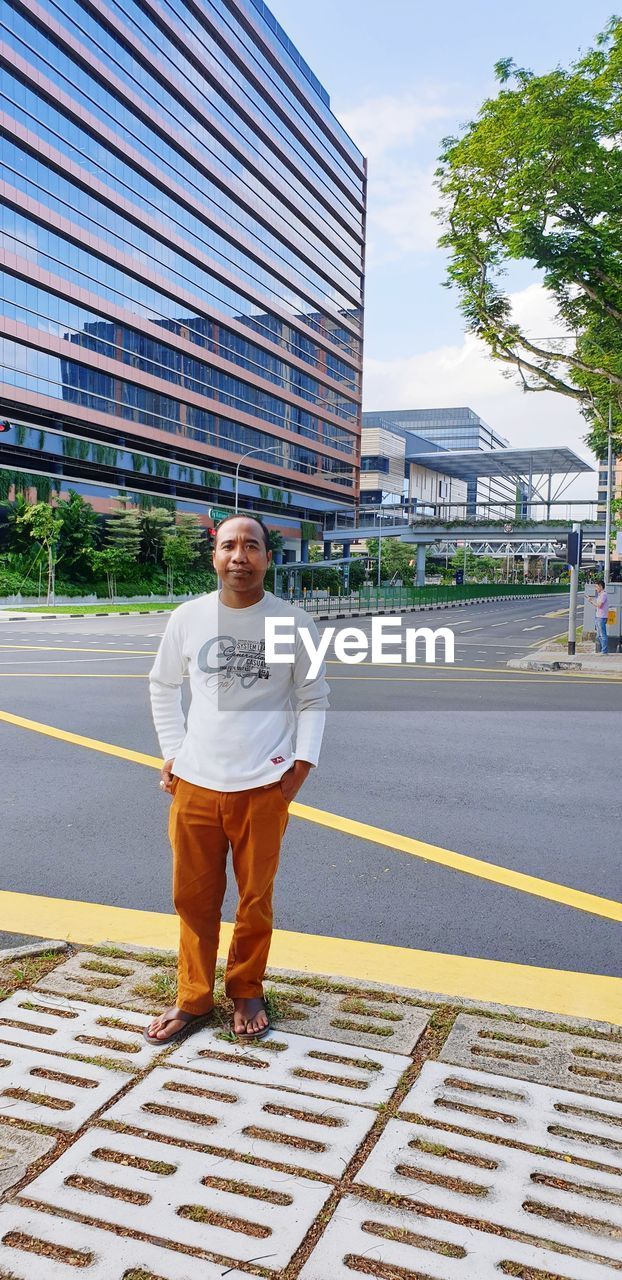 PORTRAIT OF MAN STANDING IN CITY AGAINST BUILDING