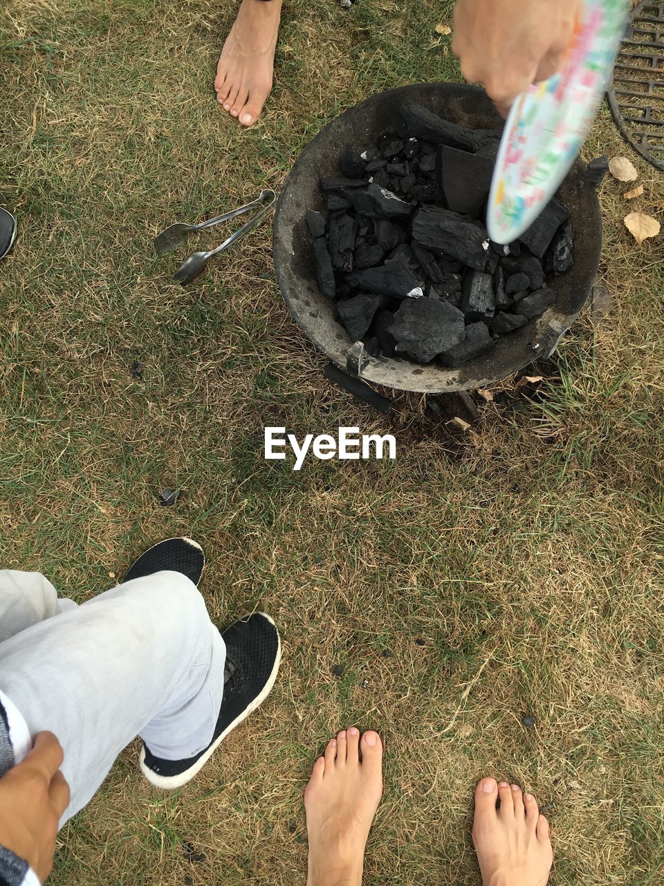 Low section of people by fire pit with coals on field
