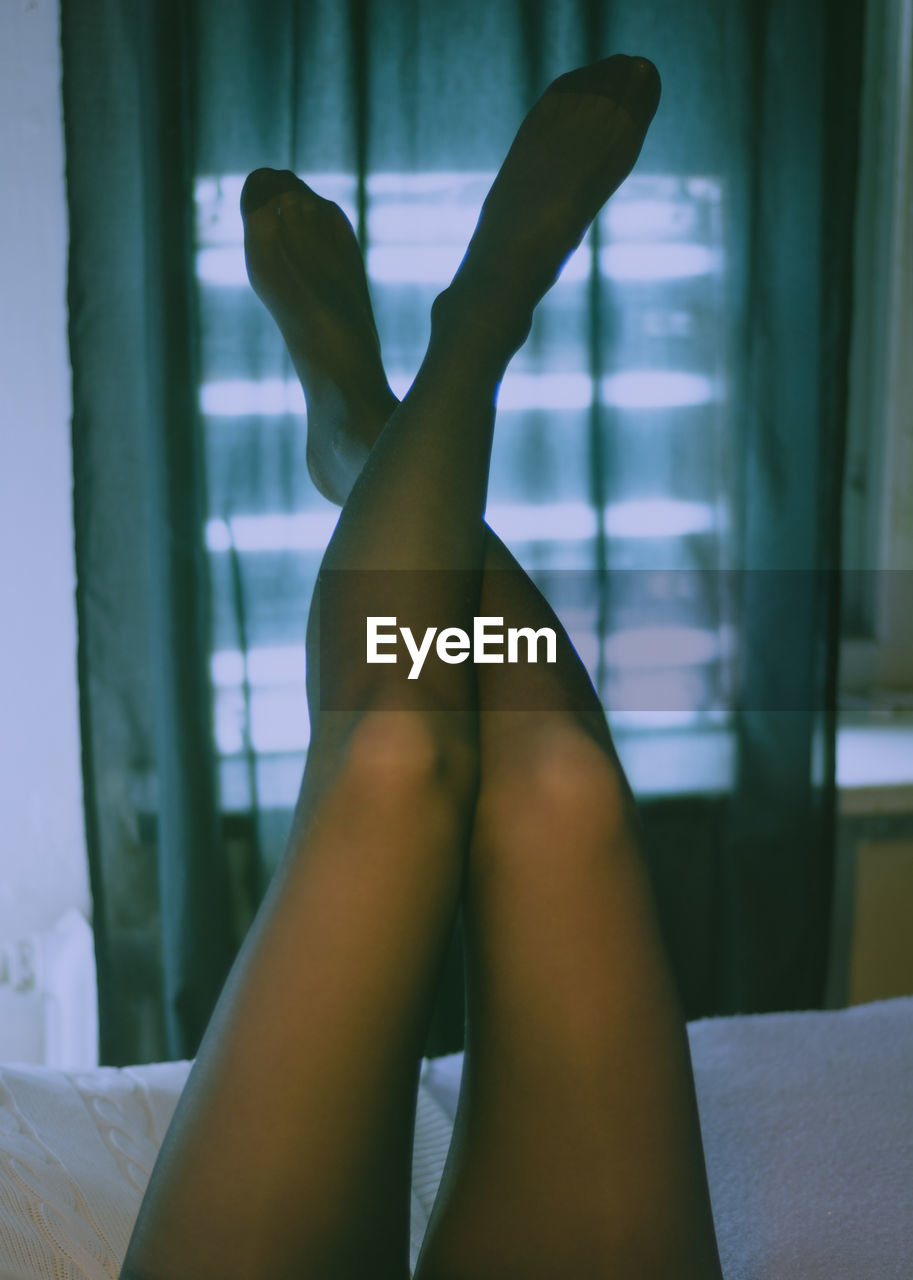 Low section of woman with feet up on bed at home