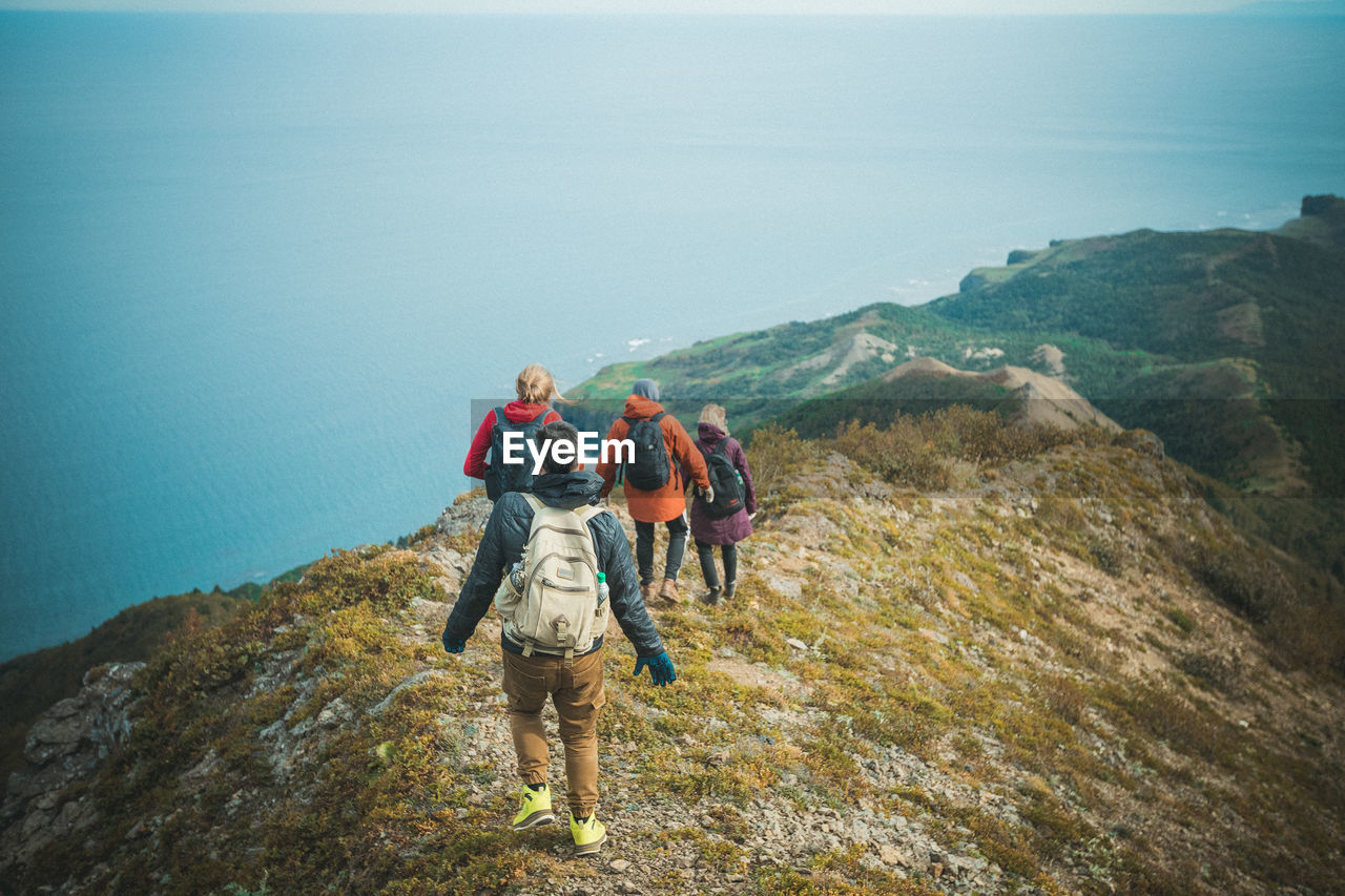 Rear view of hikers walking on mountain against sea