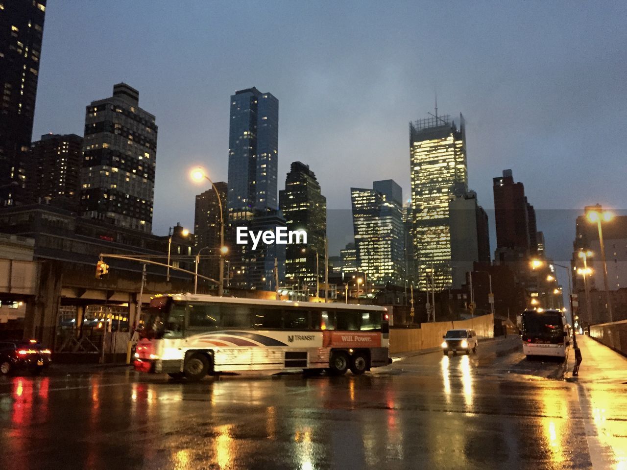 Bus on wet street with office buildings against sky at twilight in weehawken