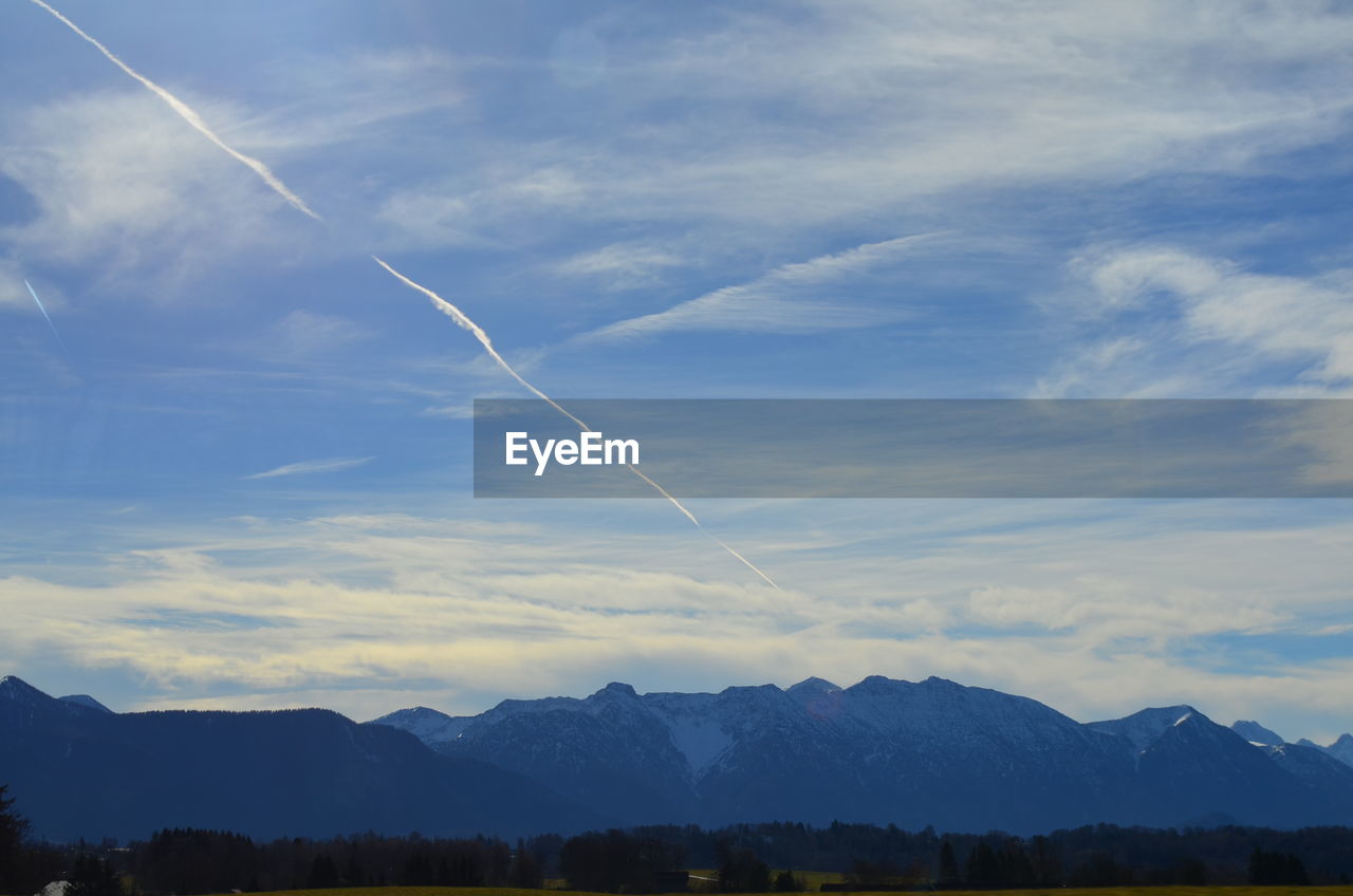 LOW ANGLE VIEW OF VAPOR TRAILS IN SKY OVER MOUNTAINS