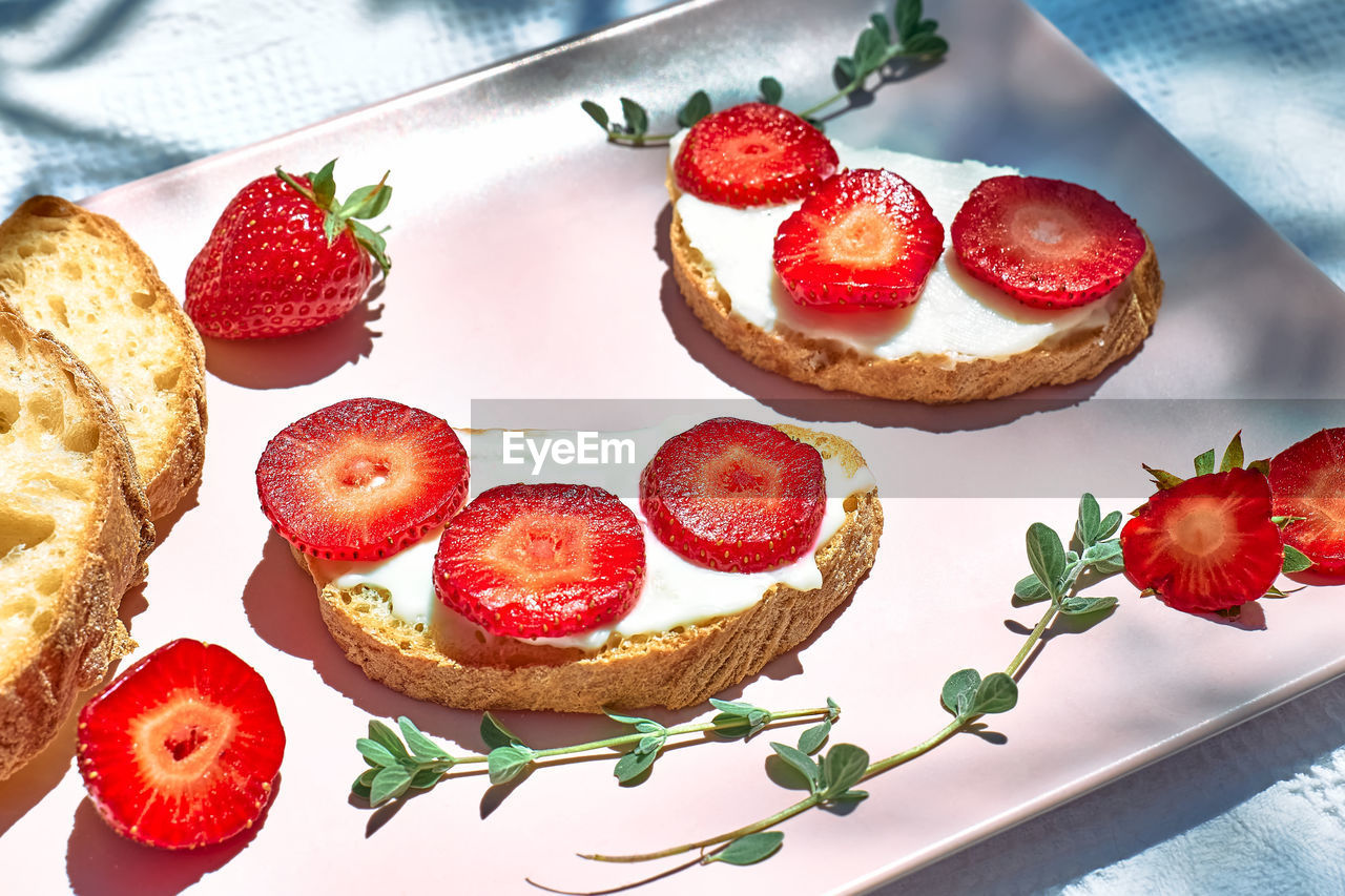 Toast bread with spread stracchino cheese and slices of ripe red strawberry on pink plate