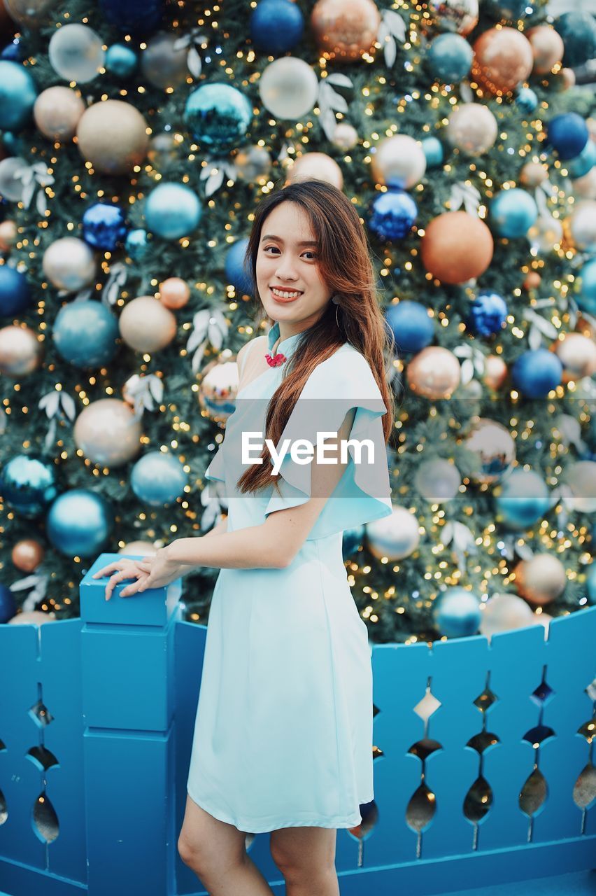 Portrait of smiling young woman standing by christmas tree outdoors