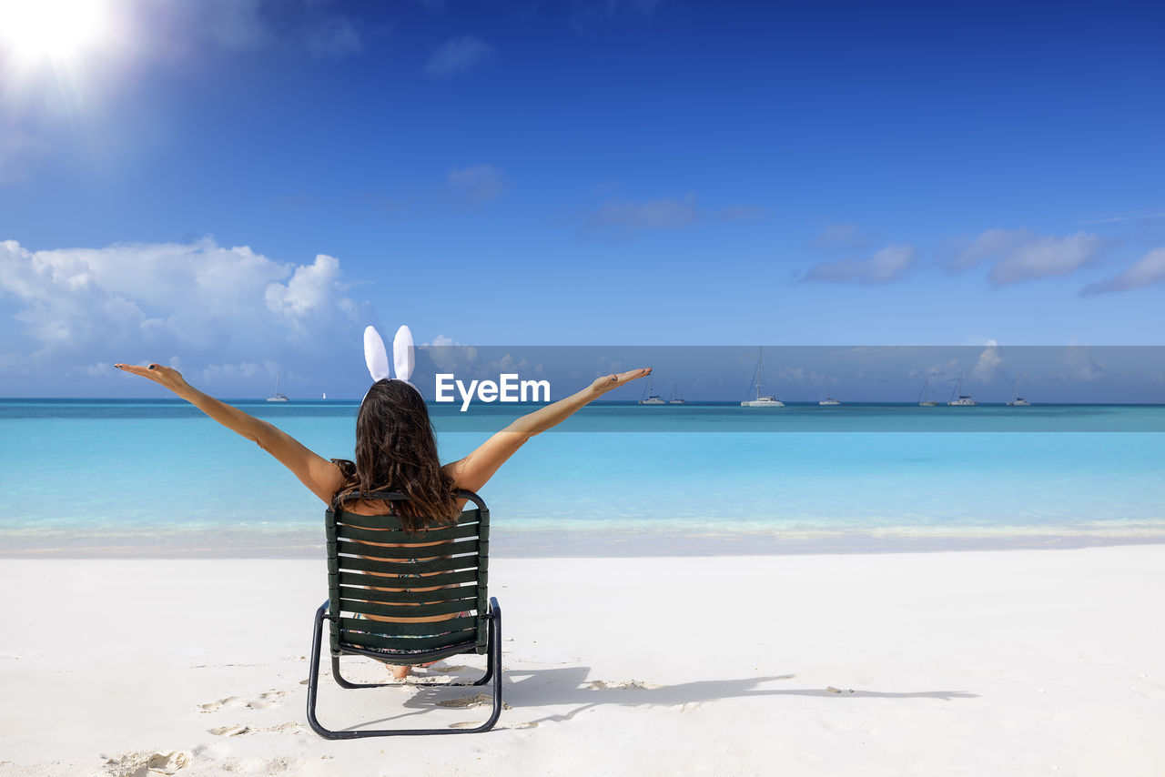 rear view of woman standing at beach against blue sky