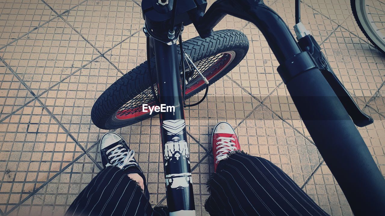 LOW SECTION OF MAN WITH BICYCLE STANDING ON TILED FLOOR