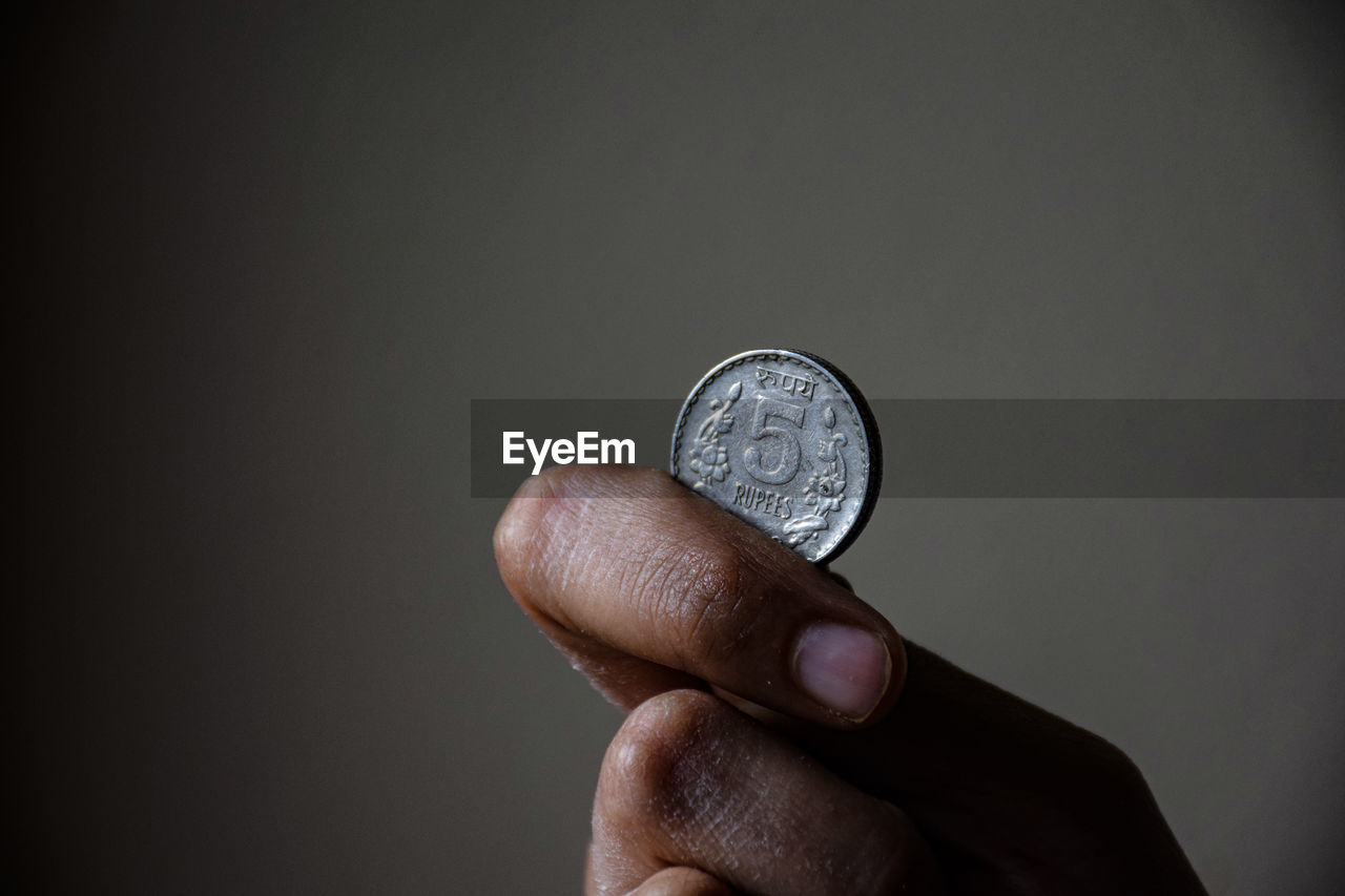 CLOSE-UP OF HAND HOLDING COIN AGAINST GRAY BACKGROUND