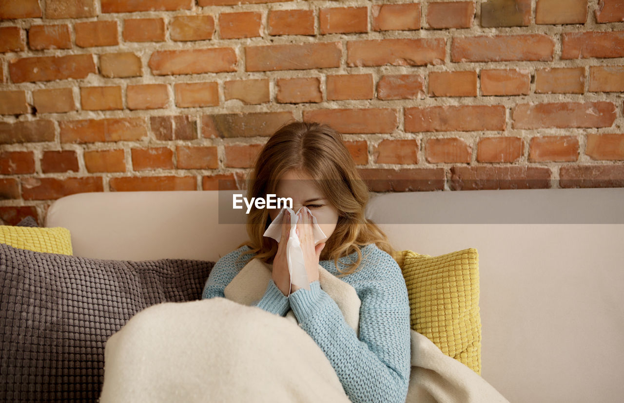 Young woman blowing nose while sitting on sofa at home