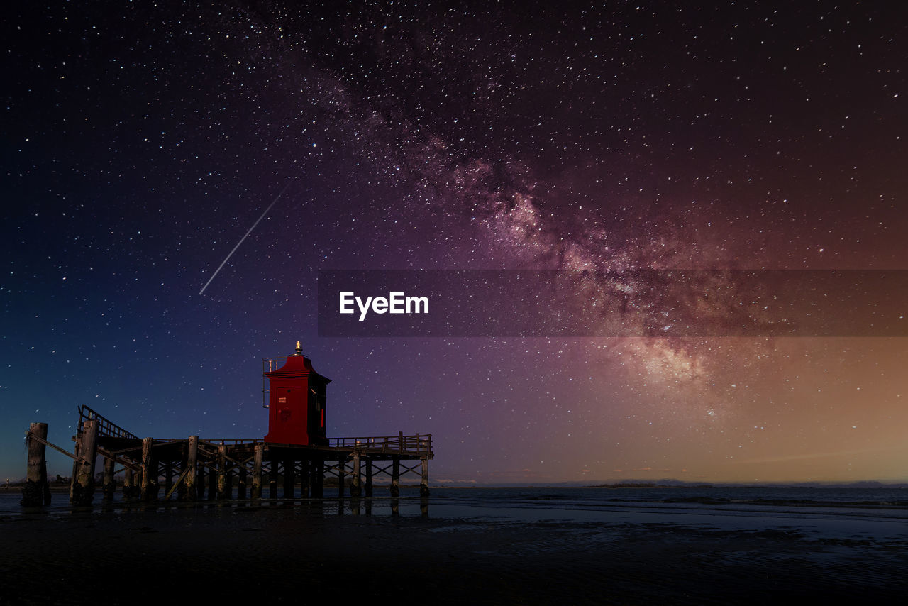 The milky way in the sky above an old wooden lighthouse on the sea