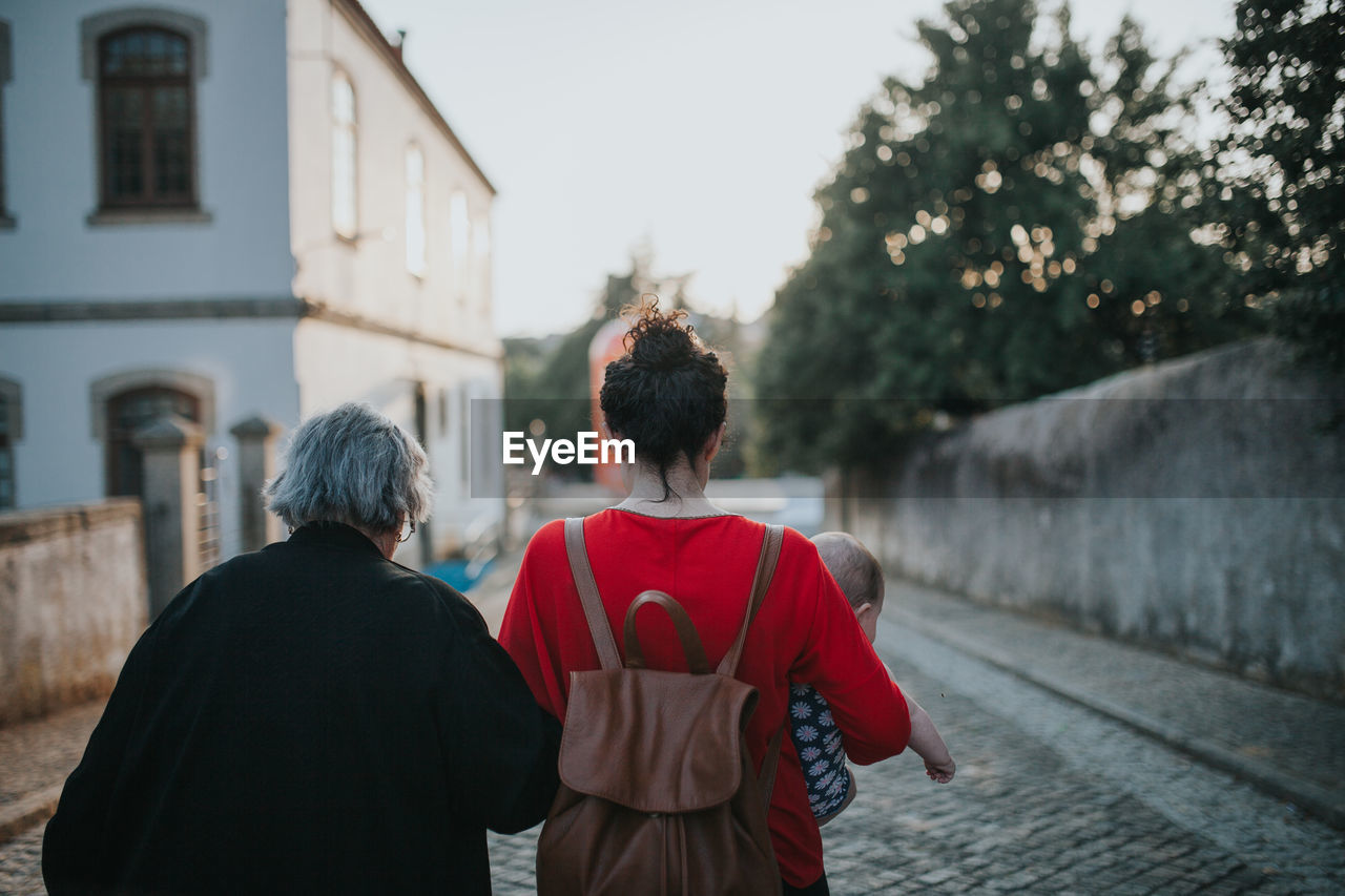 Rear view of multi-generation family walking on street against sky during sunset