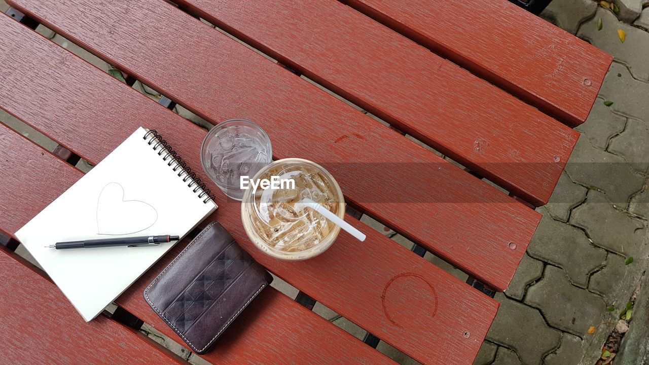 Top view of ice coffee, ice water, wallet and notebook on table