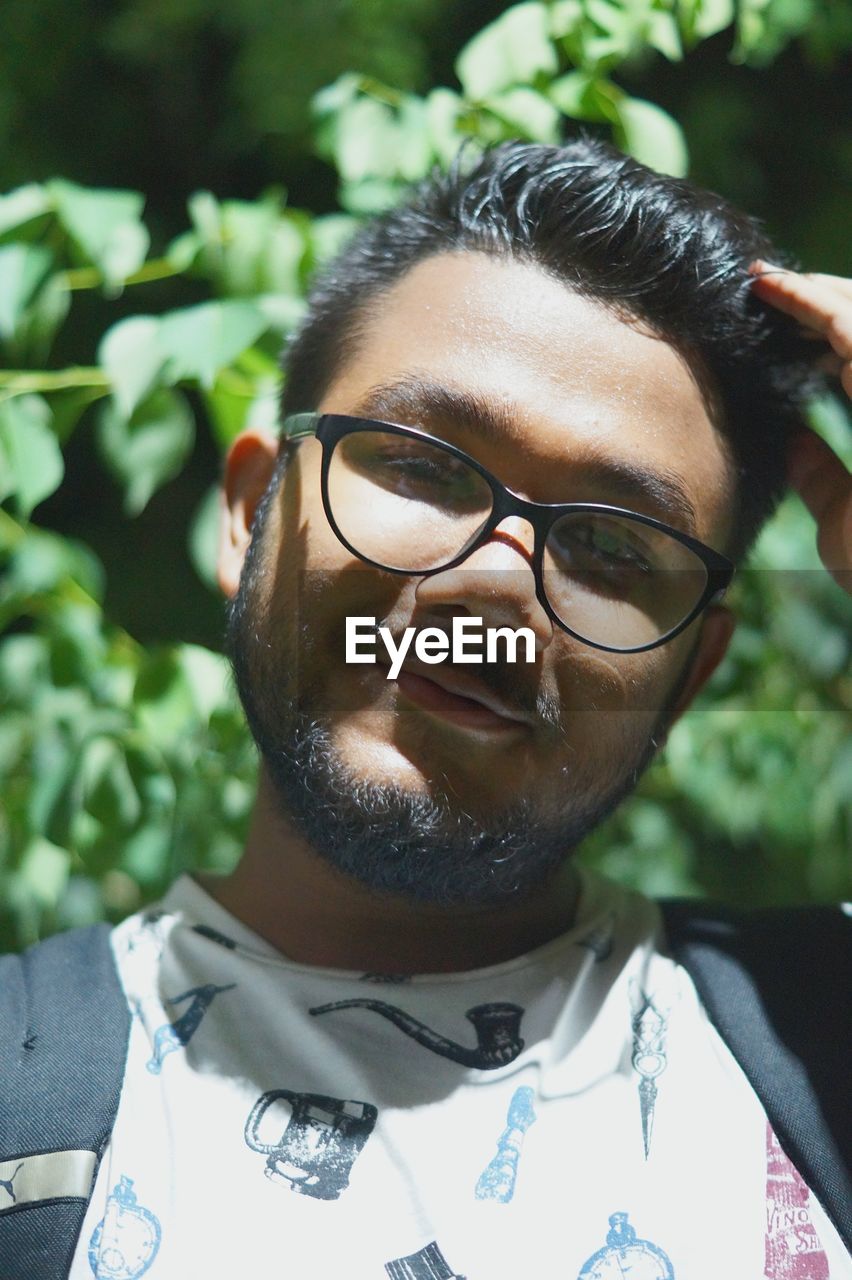 Close-up portrait of young man wearing eyeglasses against plant