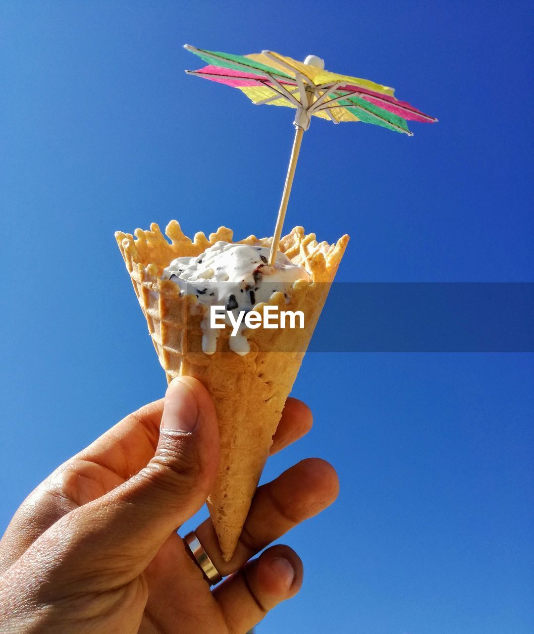 CLOSE-UP OF WOMAN HOLDING ICE CREAM AGAINST BLUE SKY