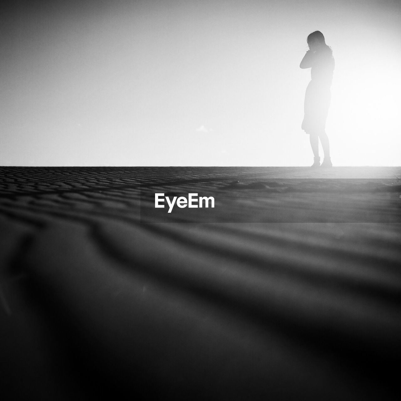 Woman standing on sand against clear sky in sunny day