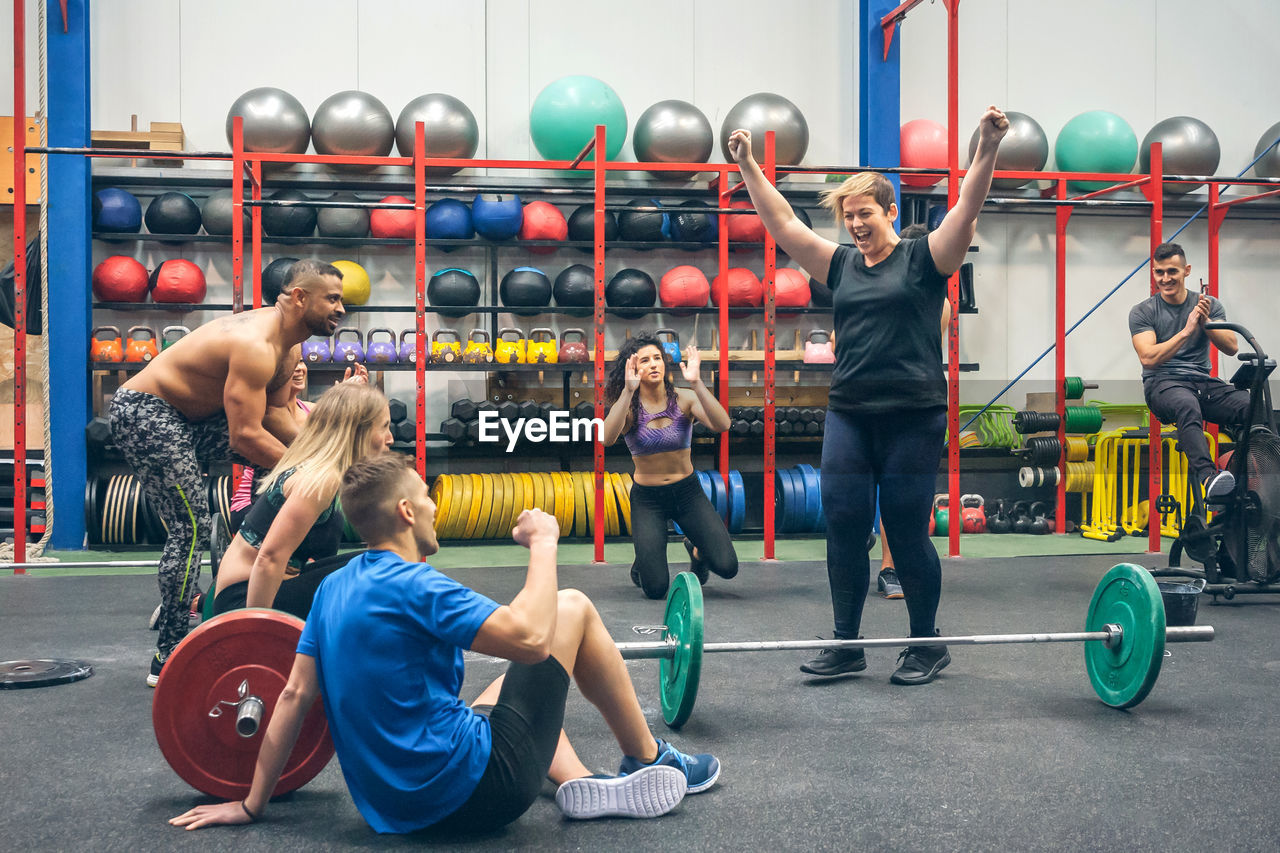 Happy woman celebrating her weightlifting achievement while her gym mates cheering her on