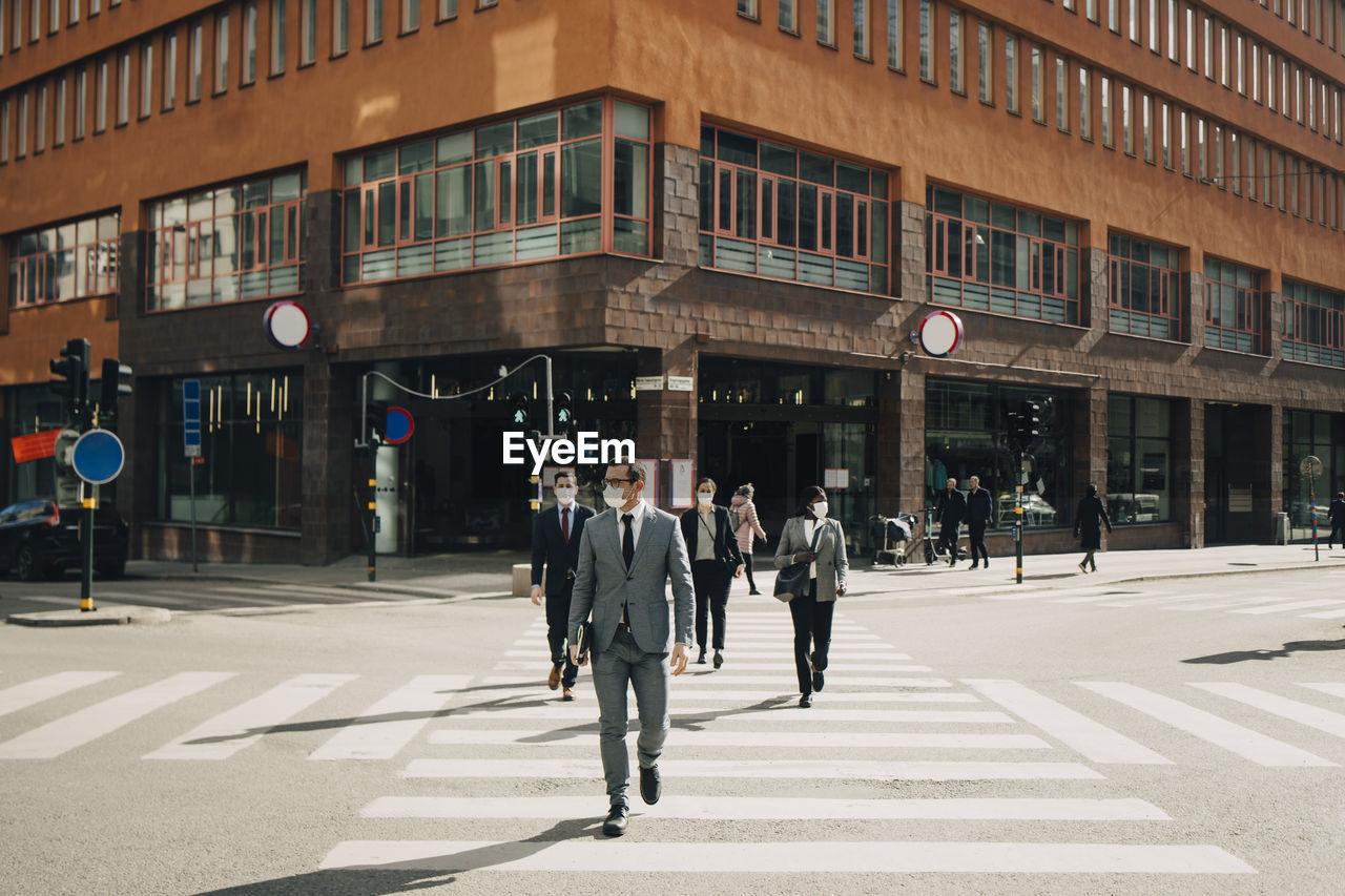 Business people crossing street on sunny day during covid-19