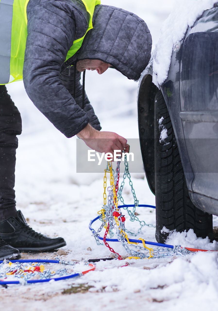 Side view of young man repairing snow covered car