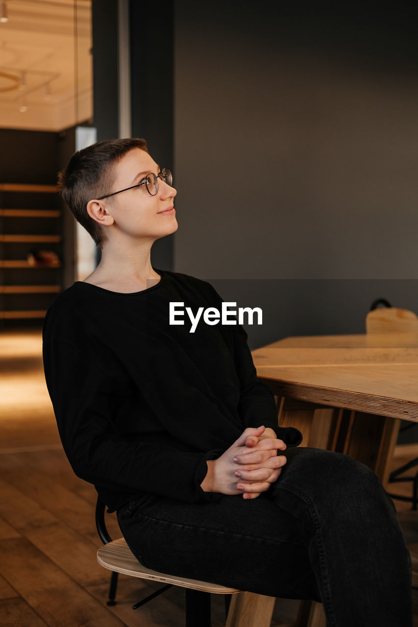 Young woman with short hair in eyeglasses and black sweater sitting at the table in office