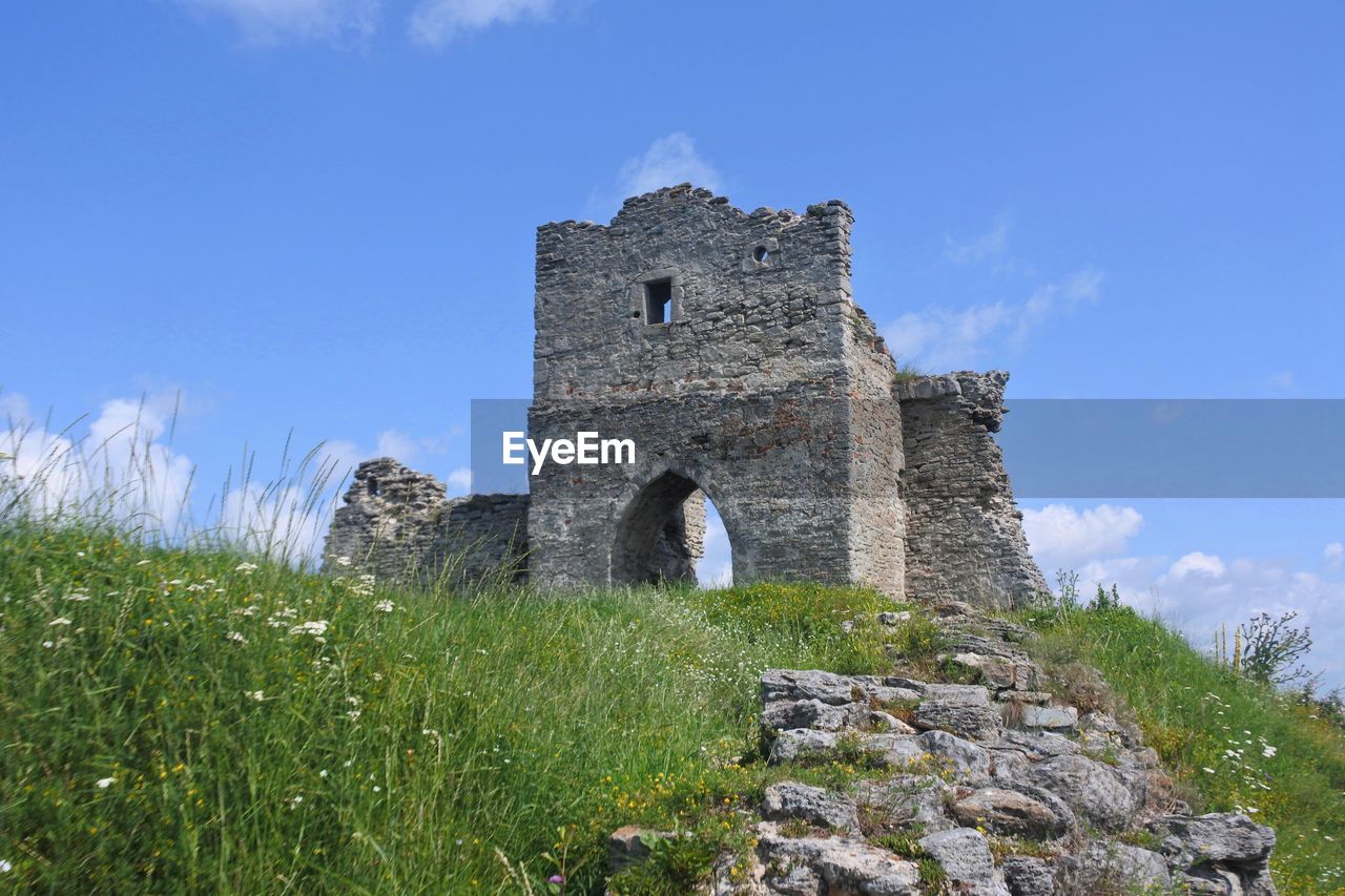 Low angle view of old ruin on hill against blue sky