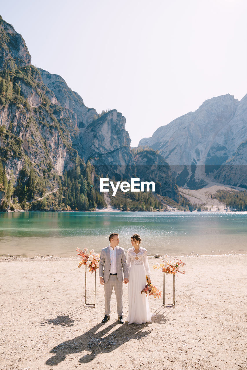 Bridegroom standing on lakeshore against clear sky