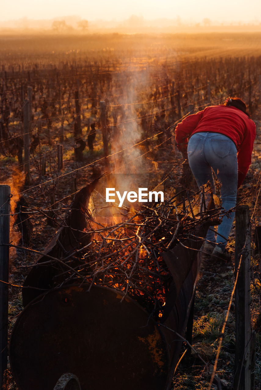 REAR VIEW OF MEN ON FIRE IN FIELD AGAINST SKY