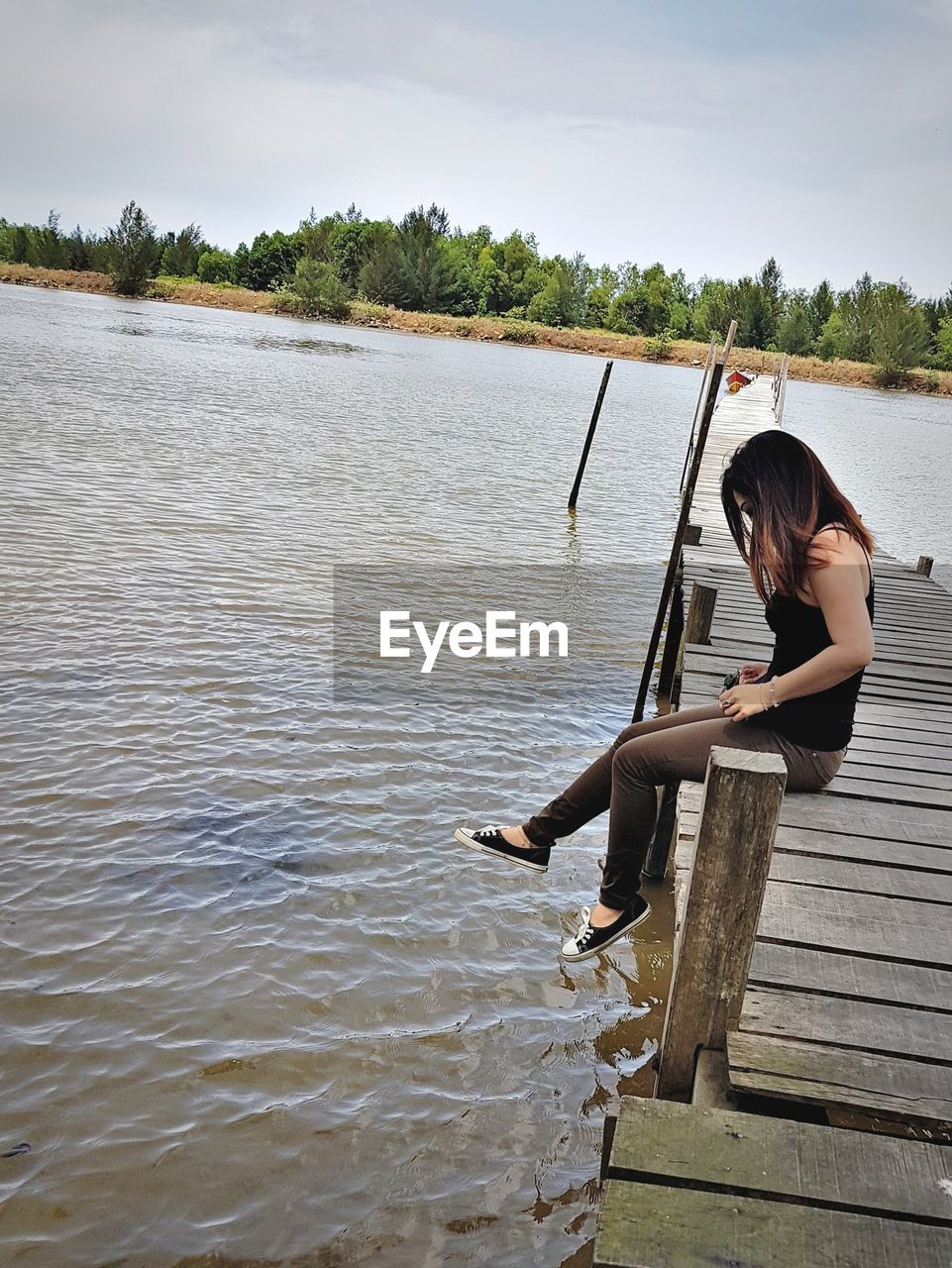 WOMAN SITTING AT LAKE AGAINST SKY