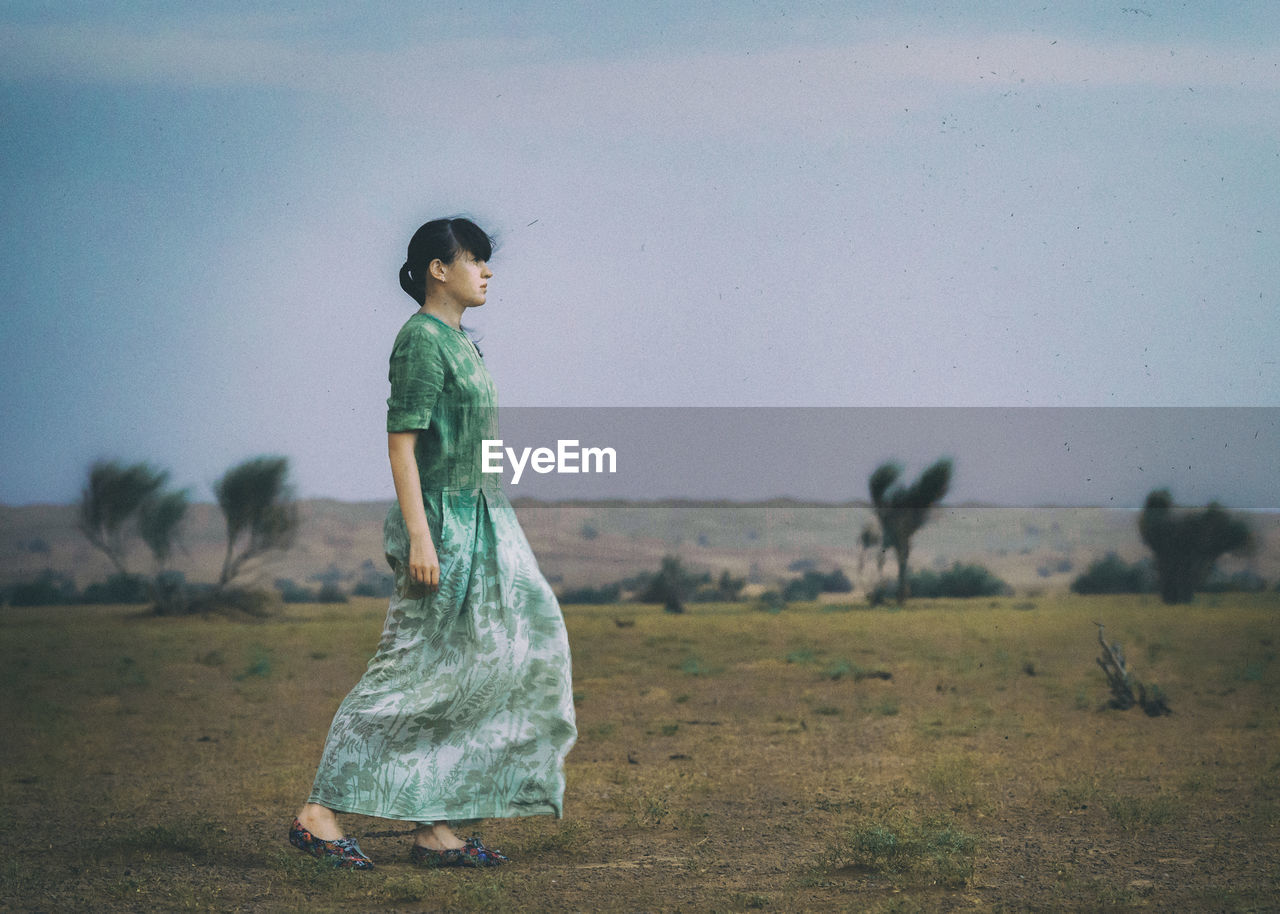 FULL LENGTH OF YOUNG WOMAN STANDING ON FIELD