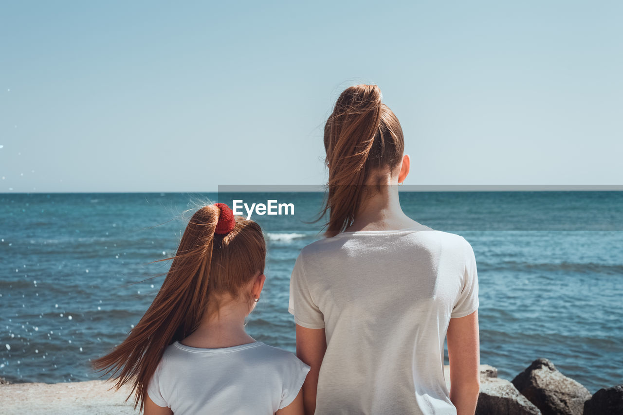 Rear view of female friends standing at beach against clear sky