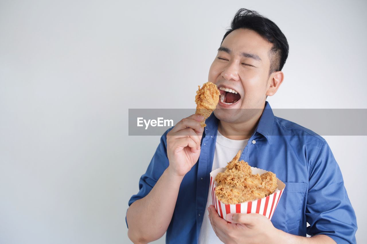 Happy asian man holding fried chicken bucket standing over white background with copy space.