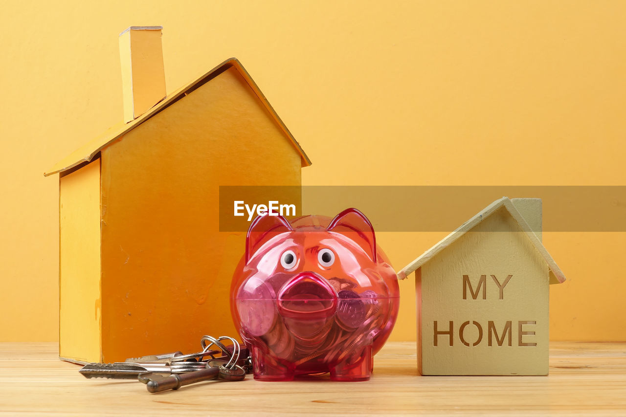 Close-up of piggy bank with model homes on table against yellow background