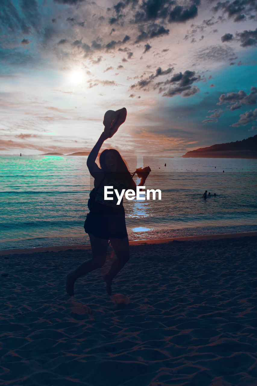 MAN JUMPING ON BEACH AGAINST SKY DURING SUNSET