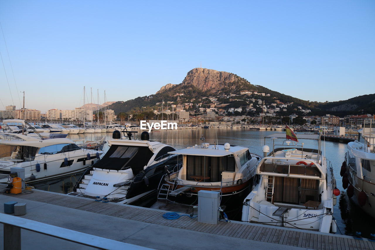 SAILBOATS MOORED IN BAY AGAINST CLEAR SKY