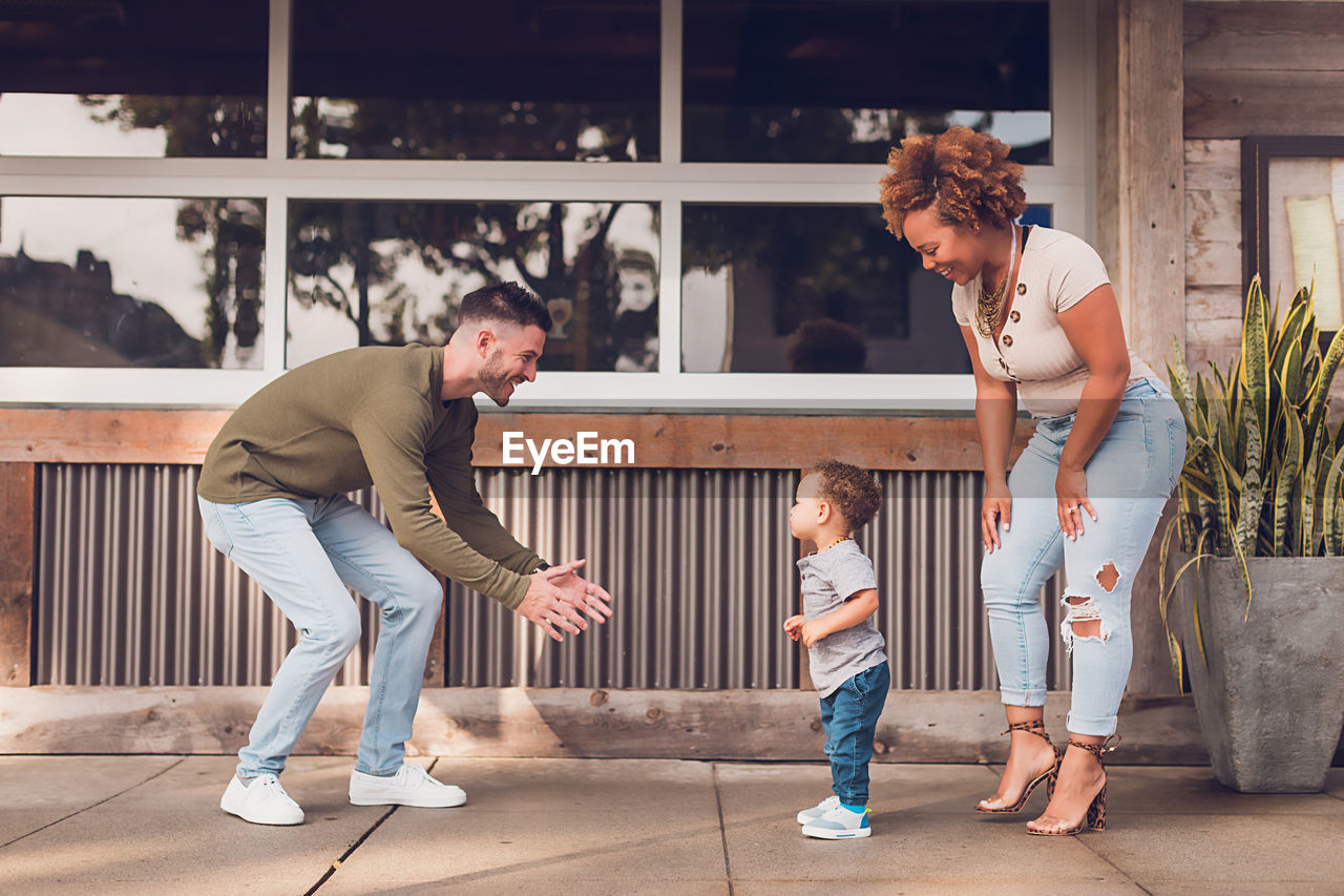 Family playing in downtown, baby boy walking to dad