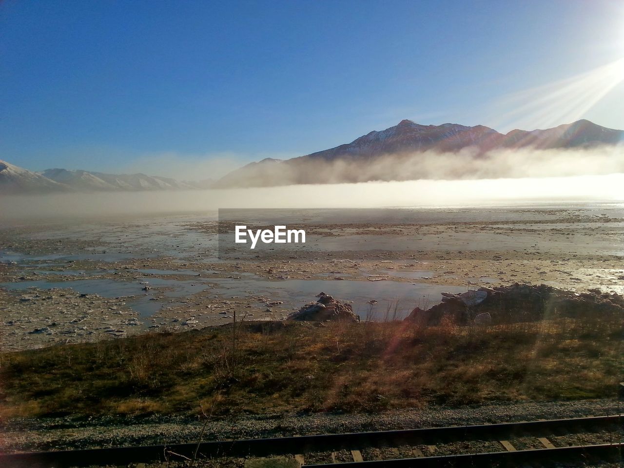 Scenic view of fog covered lake by mountains against clear blue sky